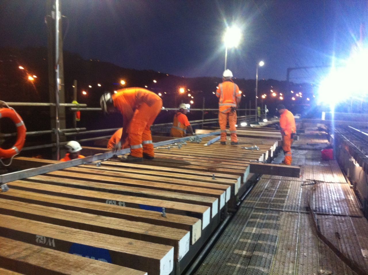 A group of construction workers are working on a bridge at night