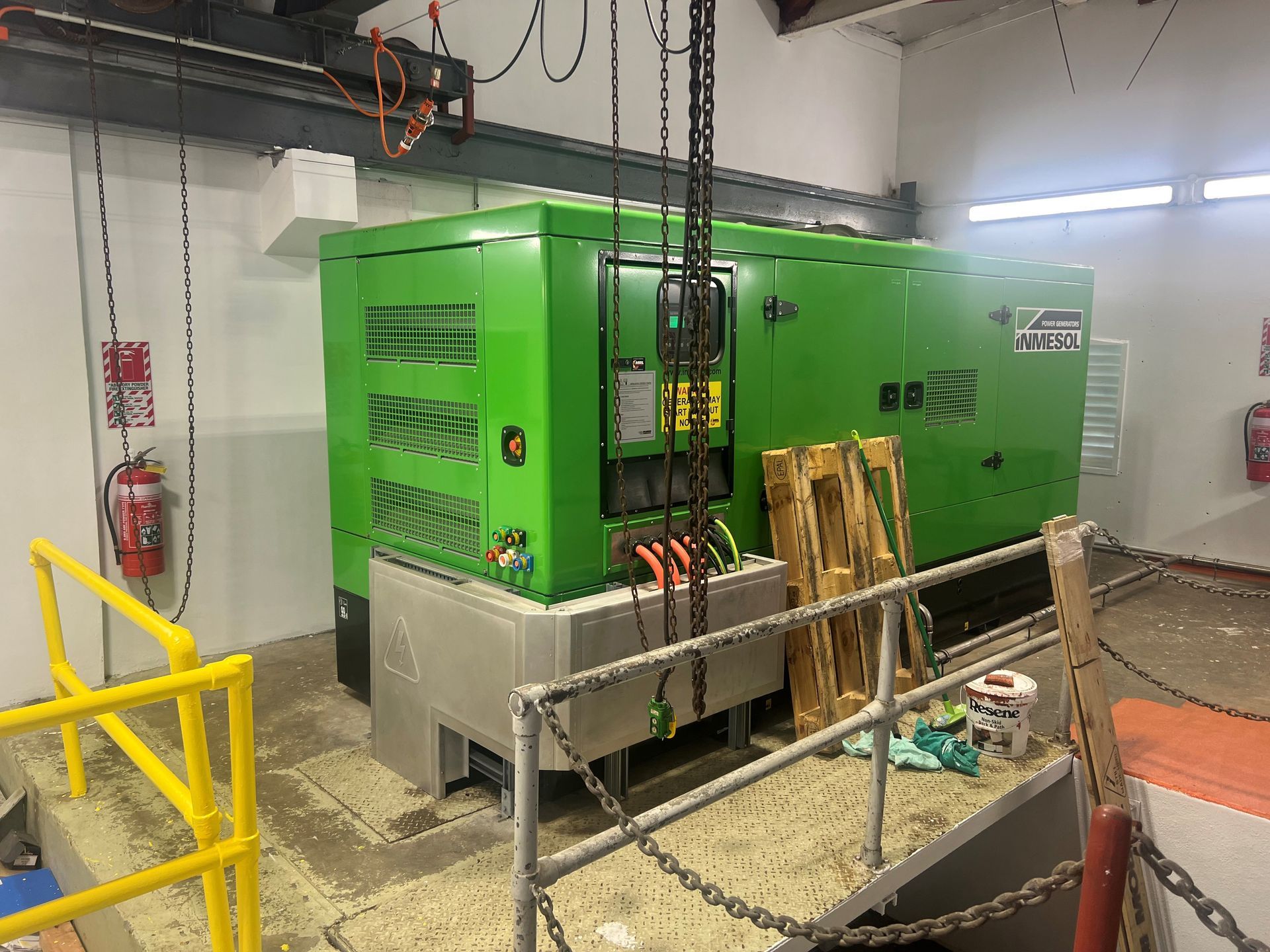 A green generator is being lifted by a crane in a room.