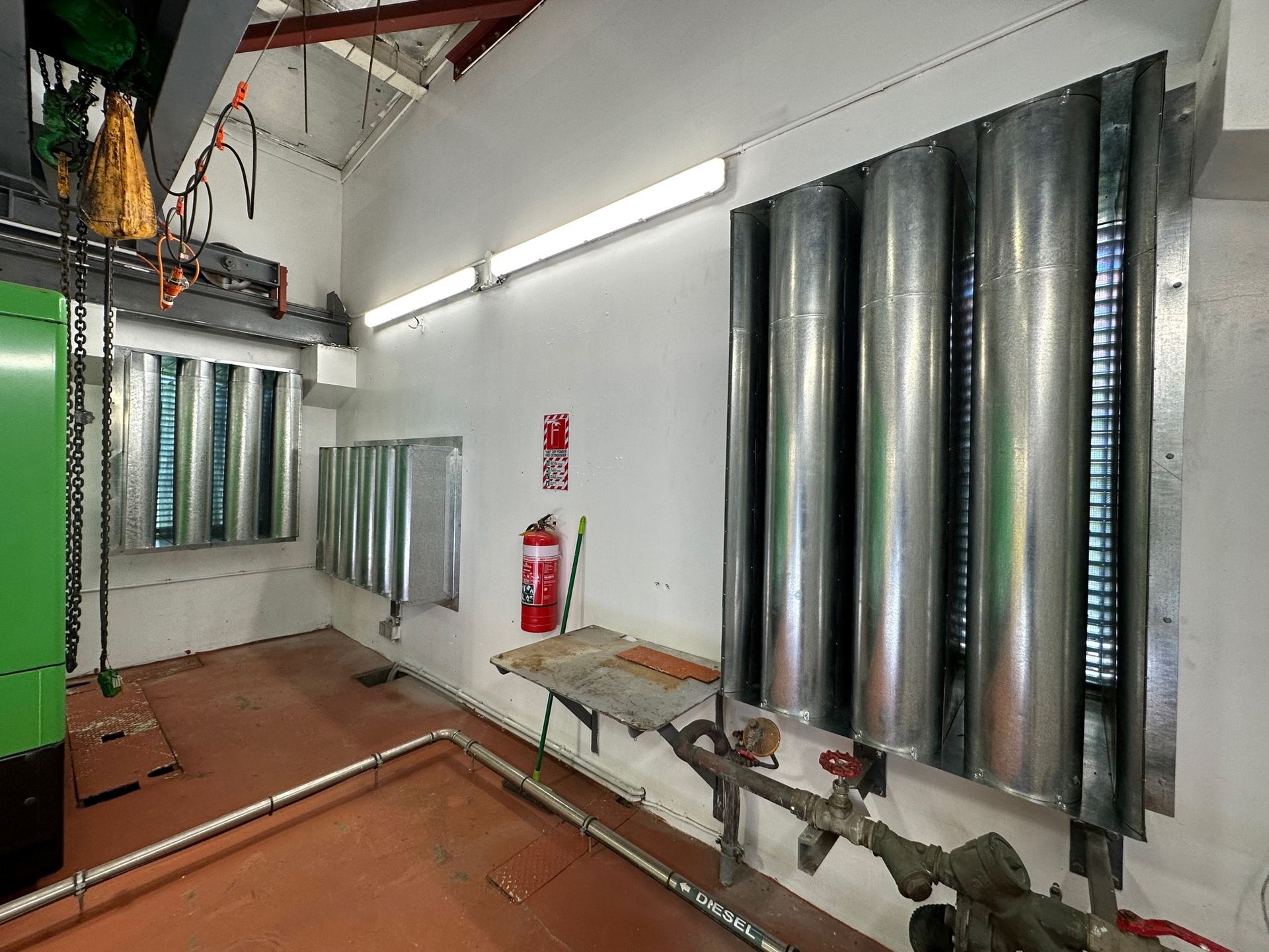 A room with a lot of pipes and a fire extinguisher on the wall.