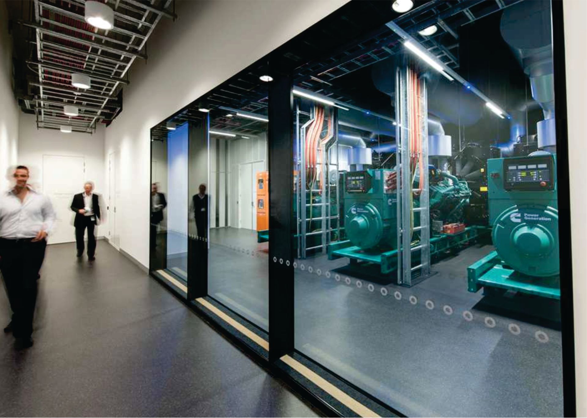 A man is walking down a hallway with a picture of a factory on the wall.