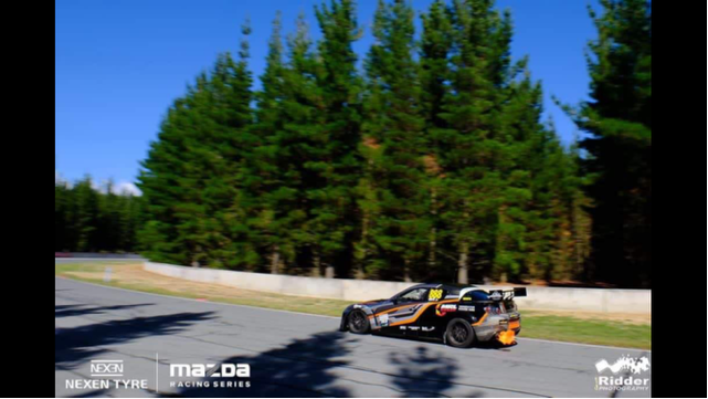 A mazda car is driving down a road with trees in the background