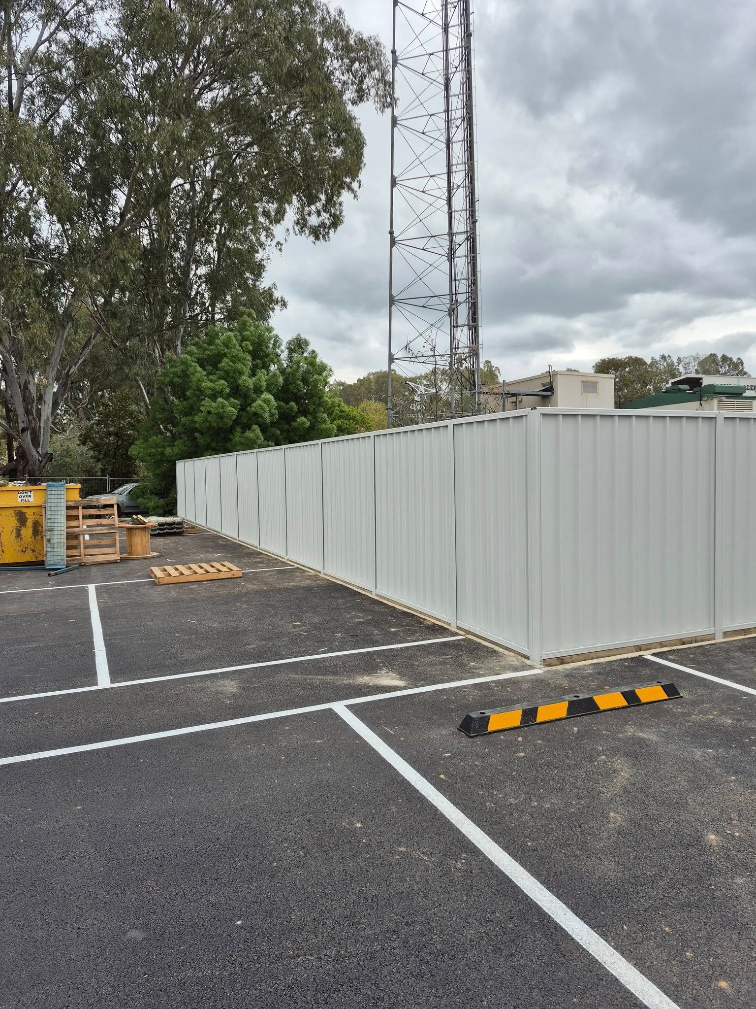 Parking lot with a white corrugated fence and a telecommunications tower — Precision Fencing & Landscaping in Thurgoona, NSW