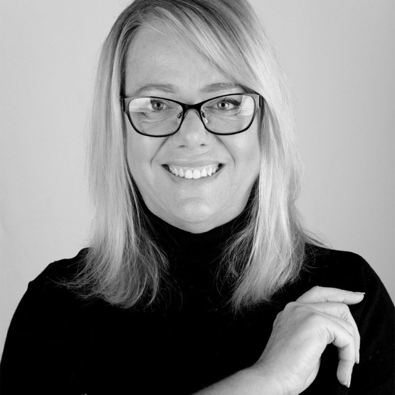 Phoebe Wright from Whitespace Marketing - a woman wearing glasses and a black turtleneck is smiling in a black and white photo .