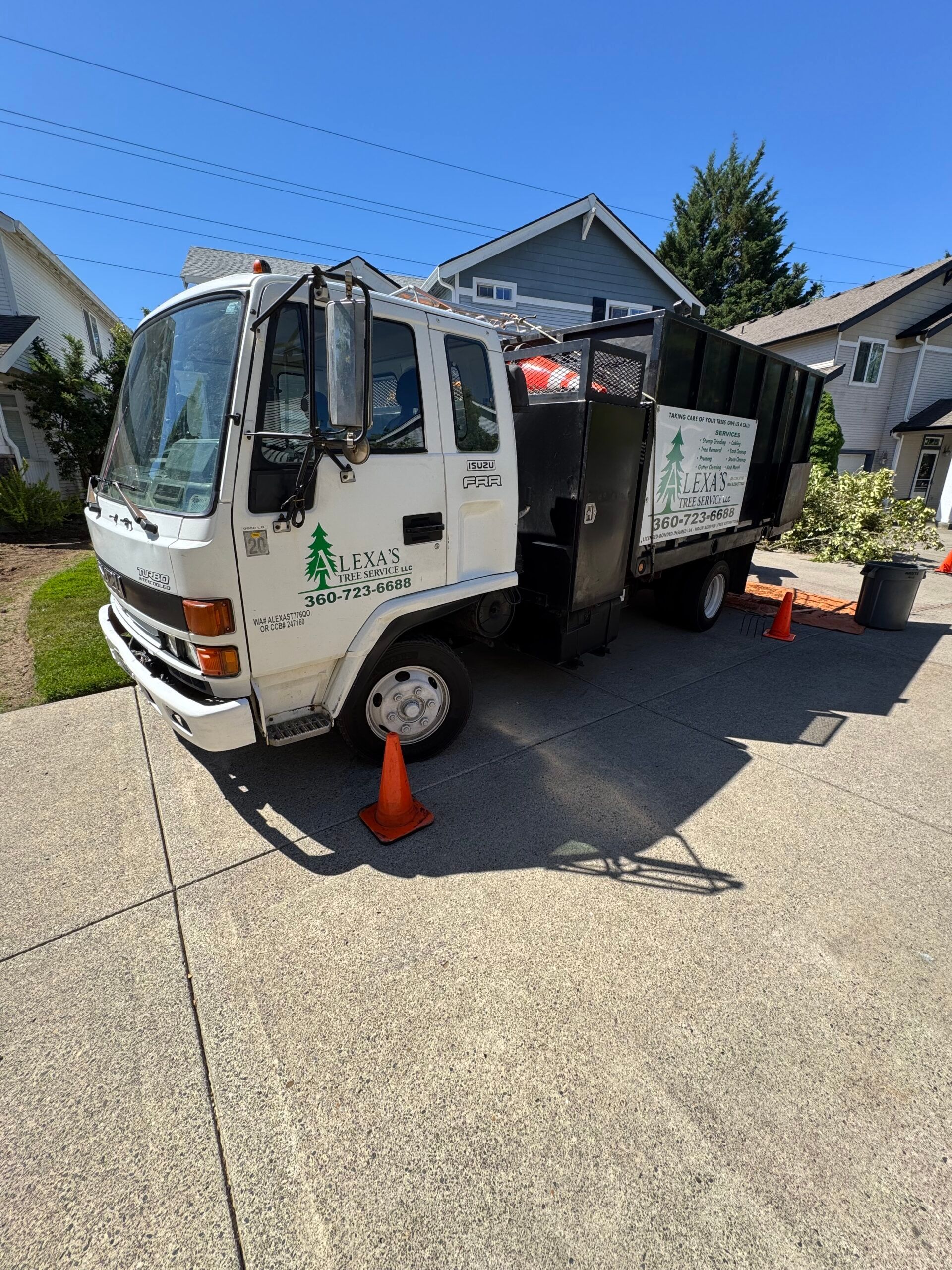 White utility truck parked on a driveway with orange cones beside it in a residential neighborhood