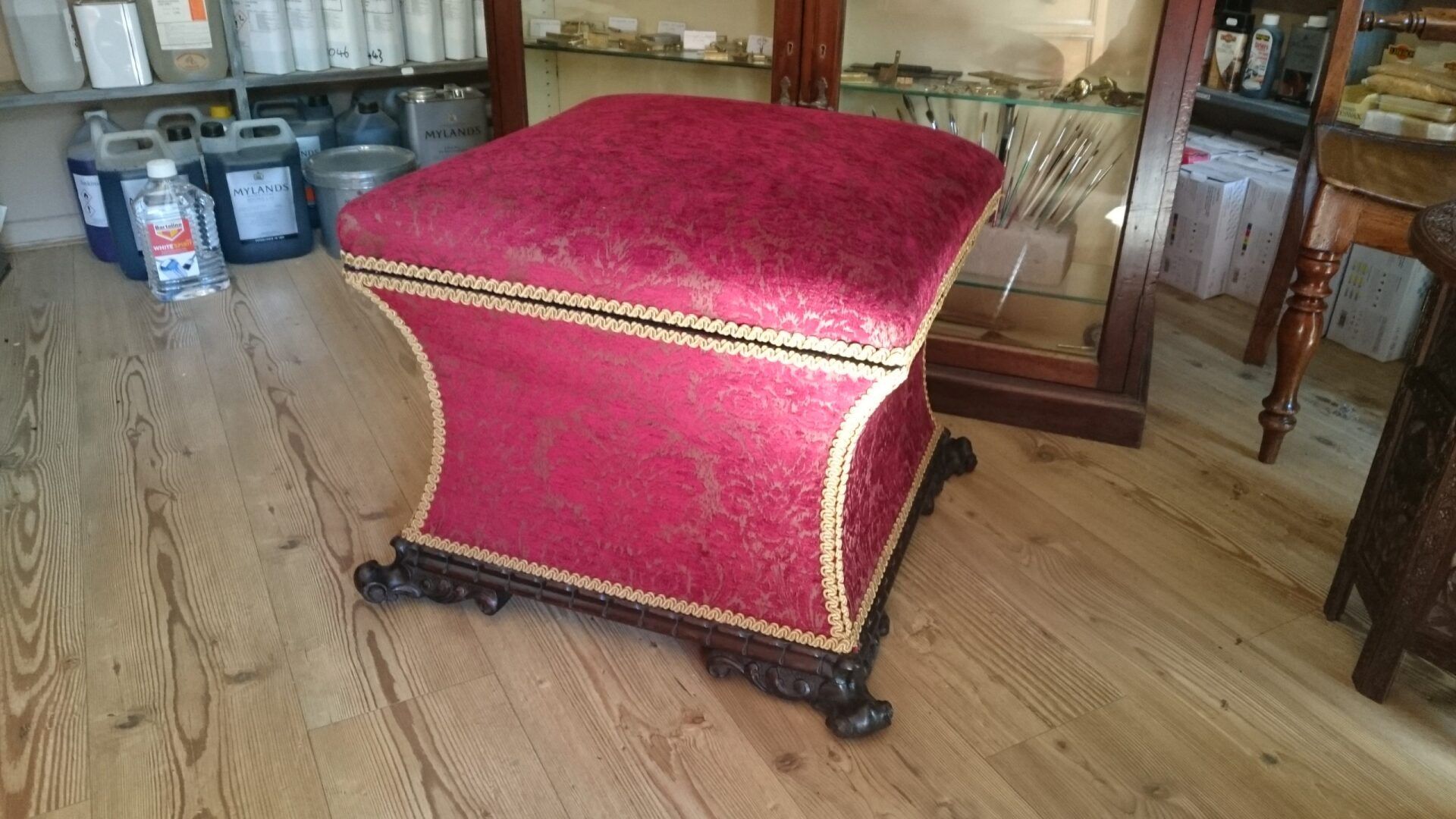 A red ottoman is sitting on a wooden floor in a room.