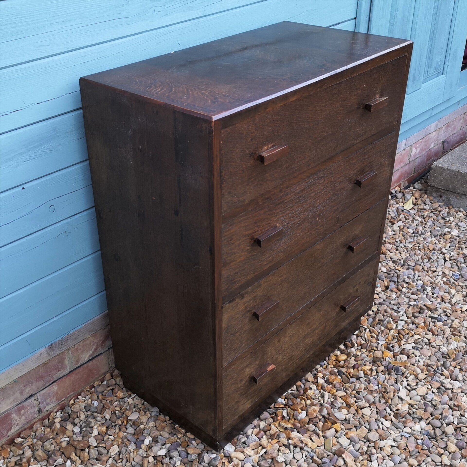 A wooden chest of drawers is sitting on gravel in front of a blue building