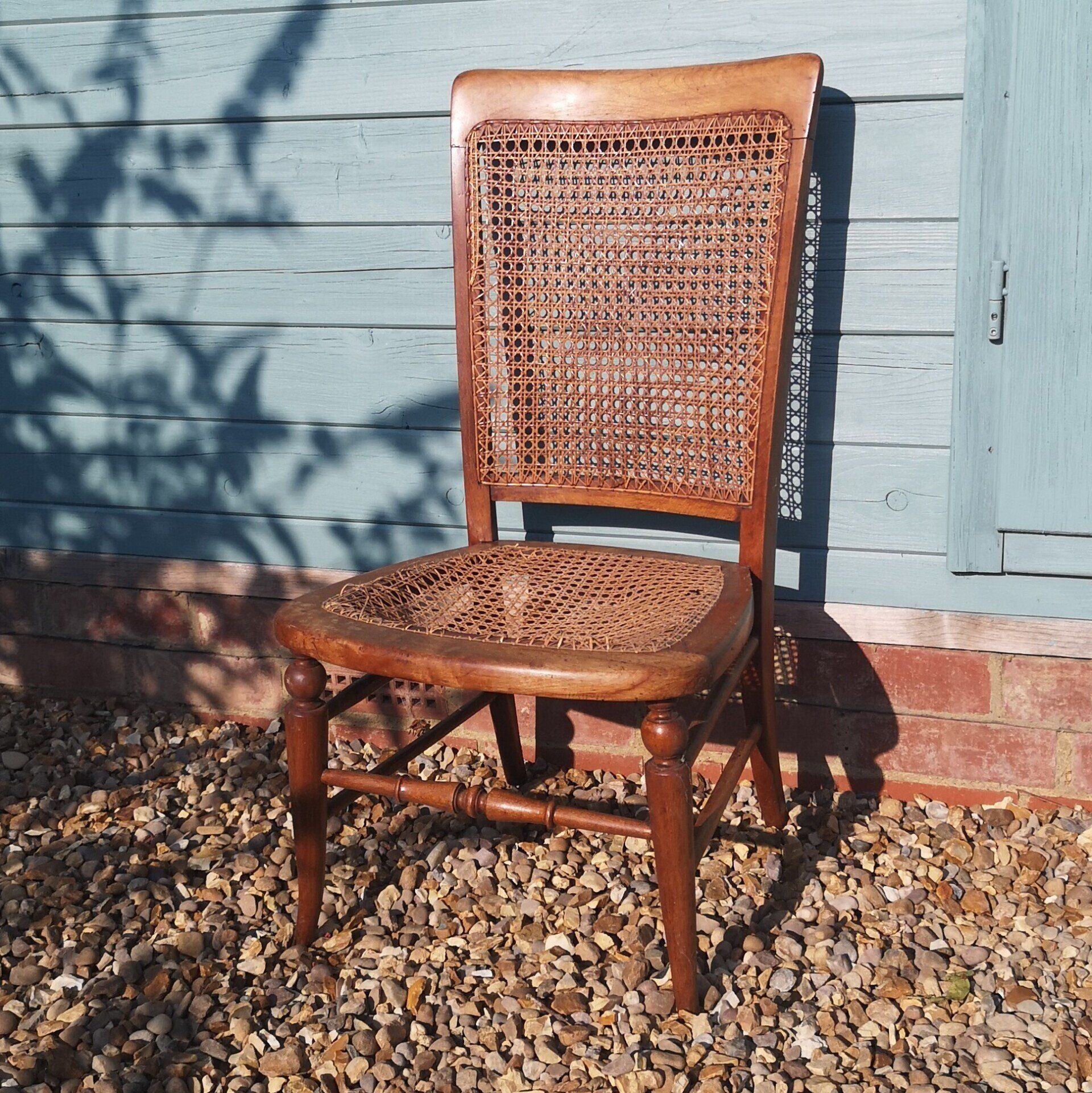 A wooden chair with a wicker seat is sitting on gravel in front of a blue building