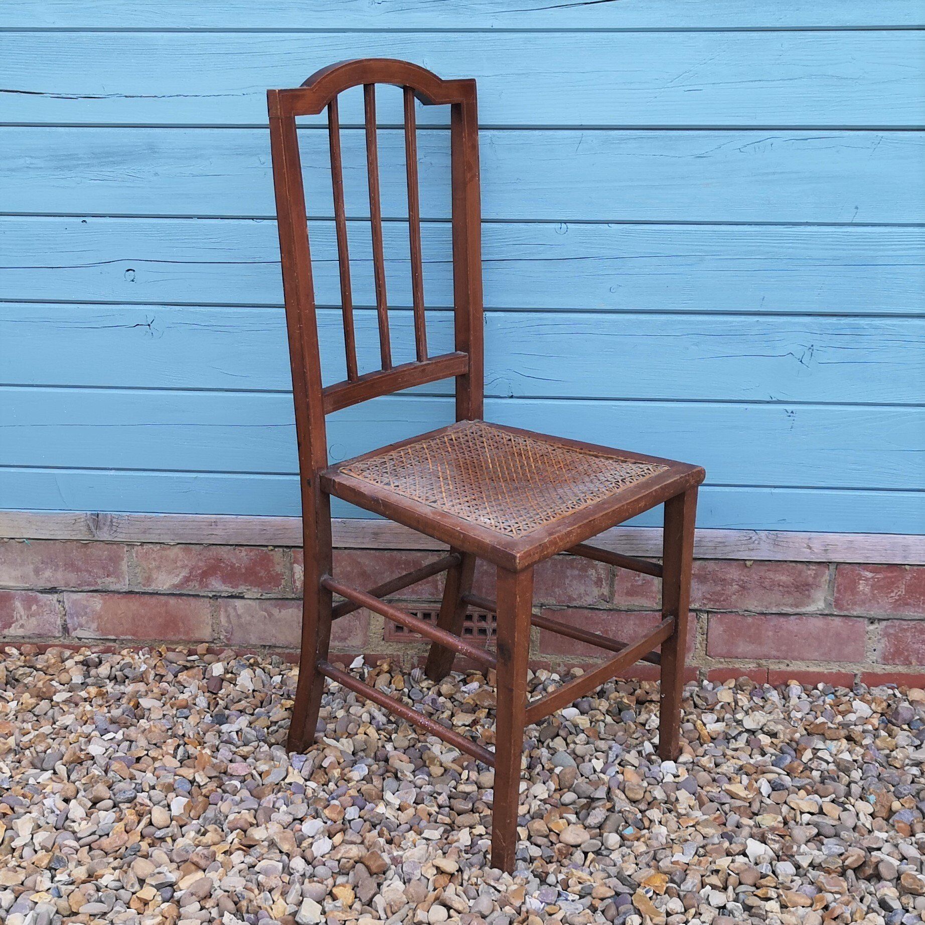 A wooden chair with a wicker seat is sitting in front of a blue wooden wall