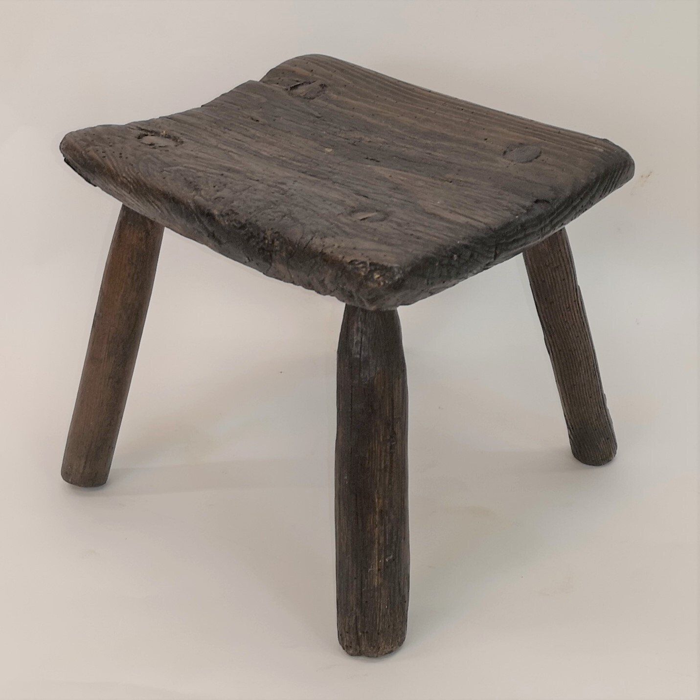 A small wooden stool with three legs on a white surface