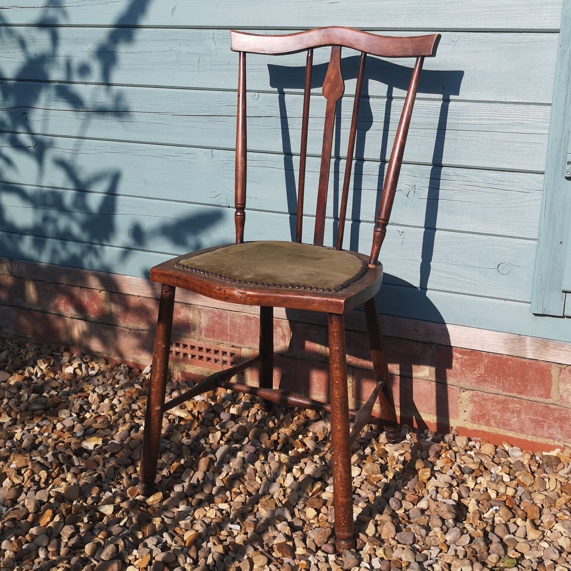 A wooden chair is sitting on gravel in front of a blue wall