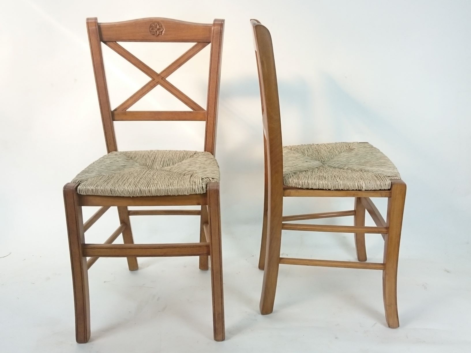 Two wooden chairs with wicker seats on a white surface