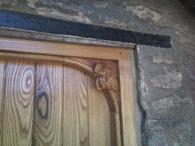 A wooden door with a carved squirrel on it is on a stone wall.
