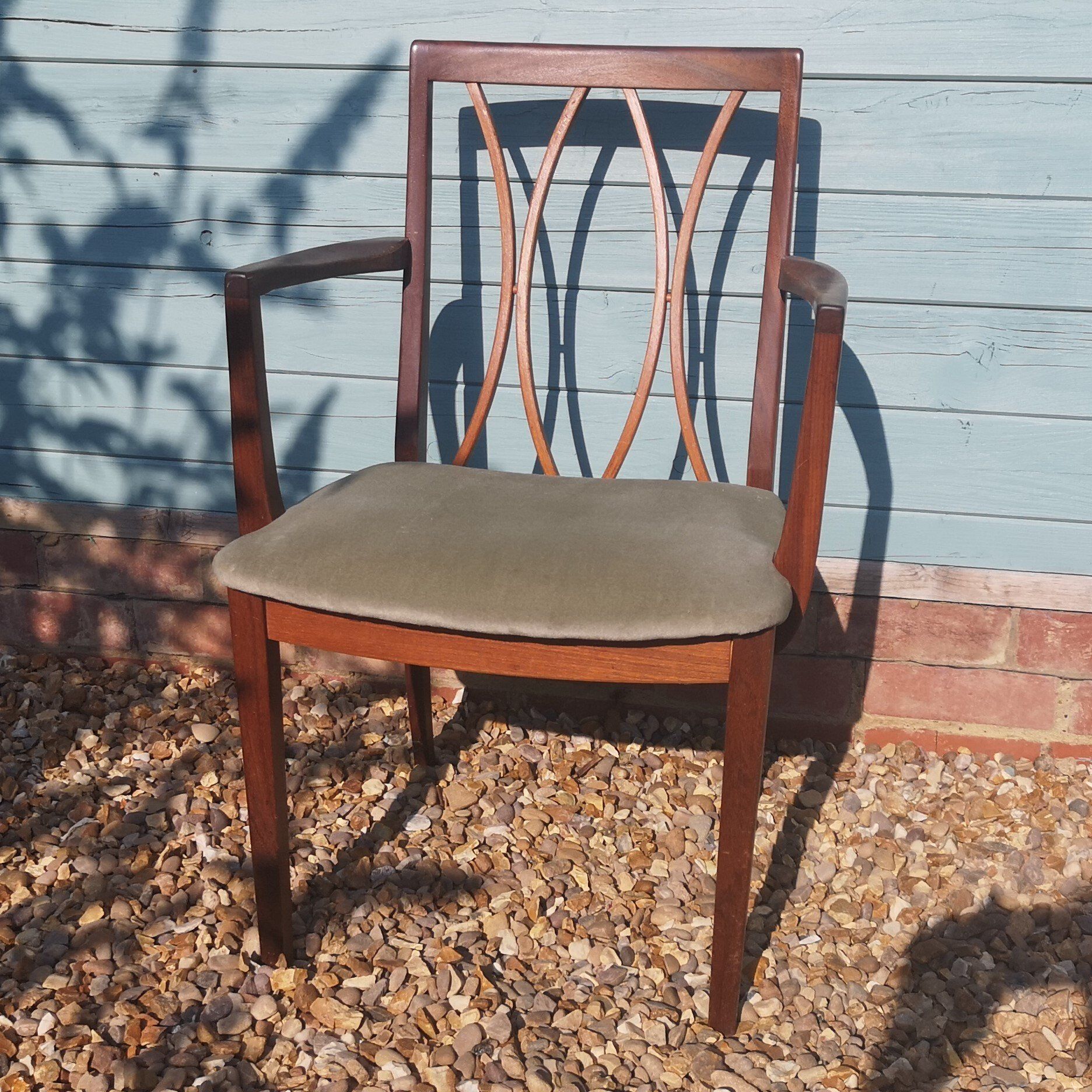 A wooden chair is sitting on gravel in front of a blue wall