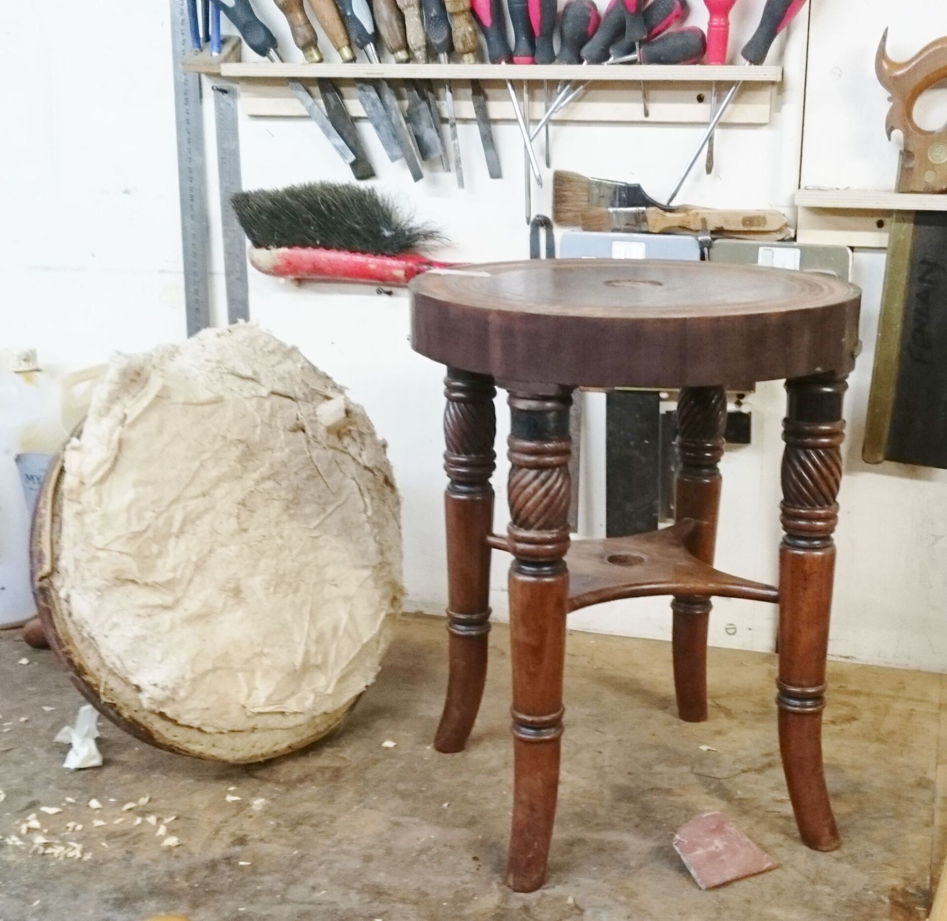 A wooden stool sits next to a drum in a workshop