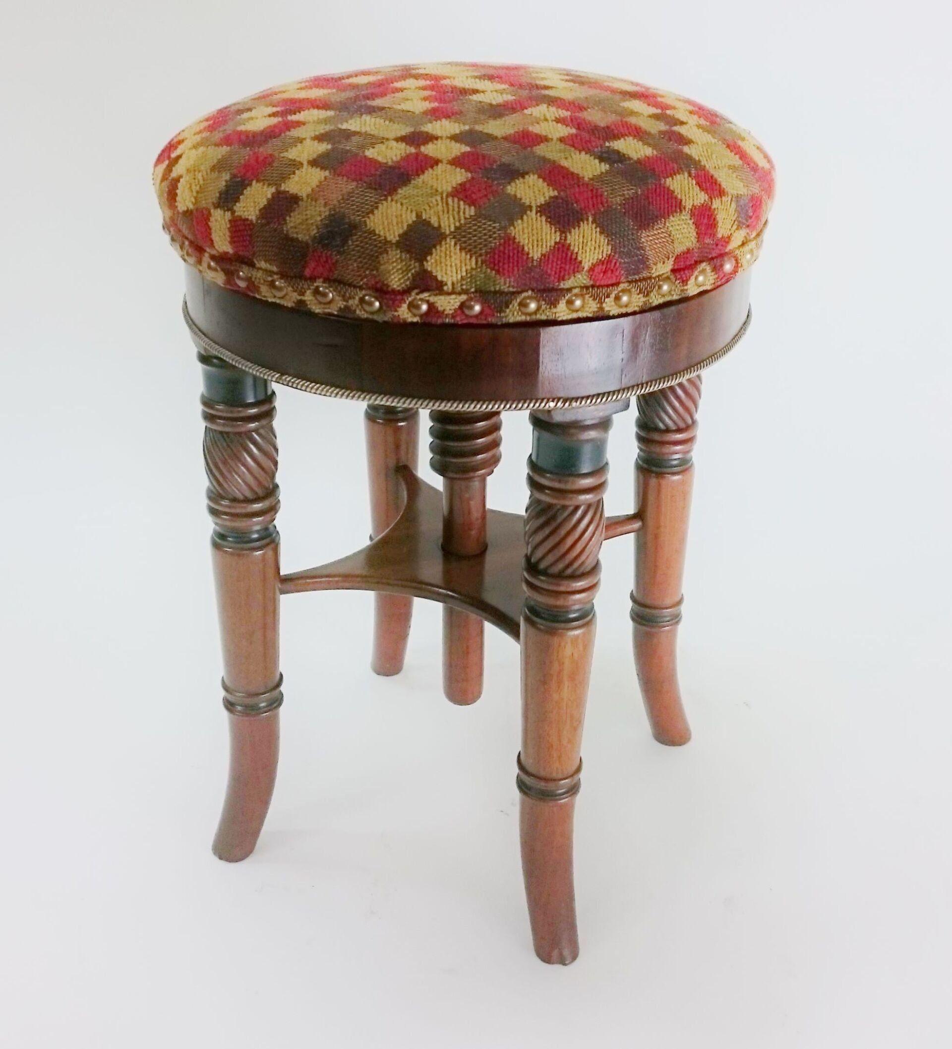 A wooden stool with a checkered cushion sits on a white surface