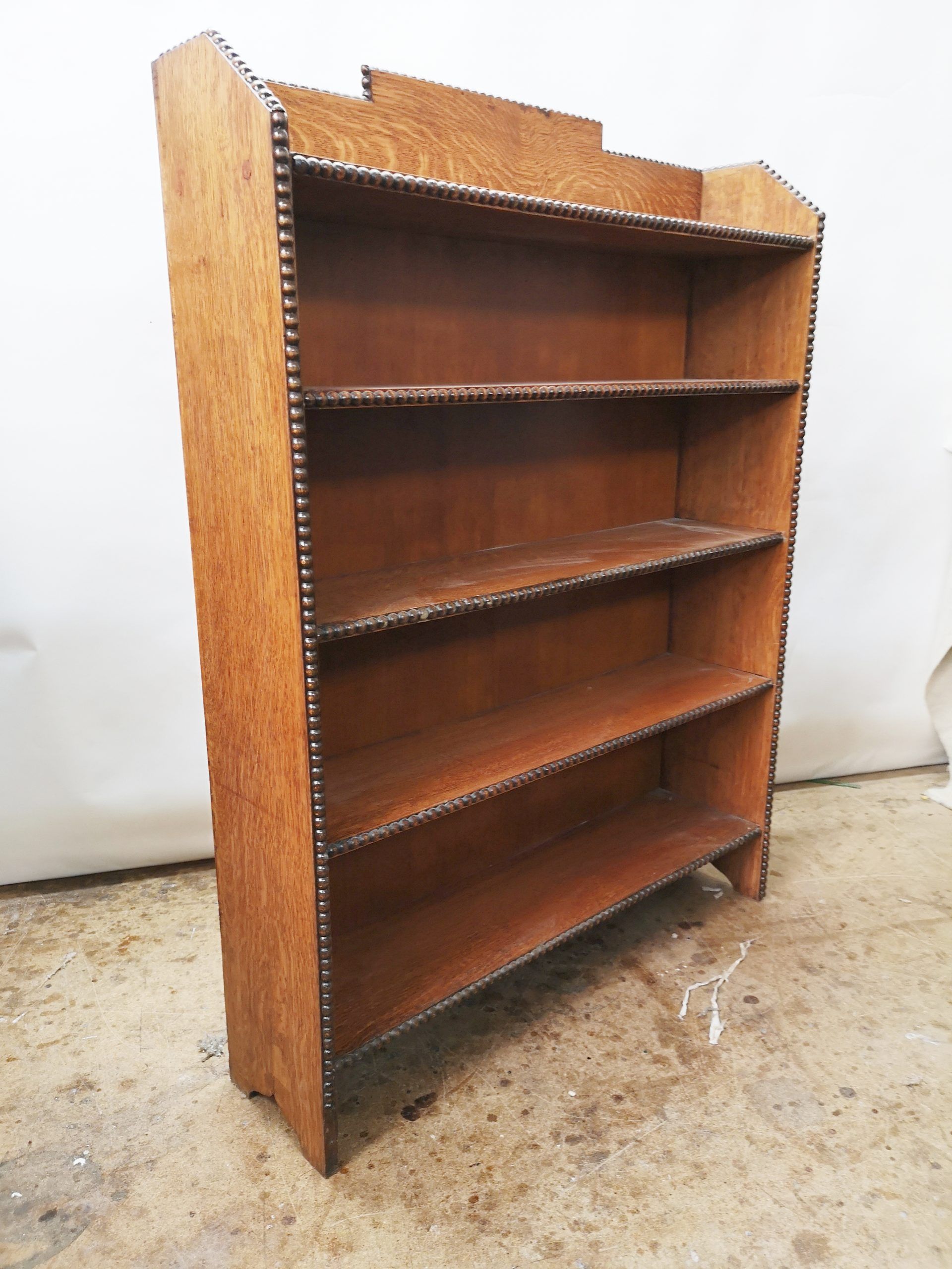 A wooden bookshelf with four shelves is sitting on a concrete floor.