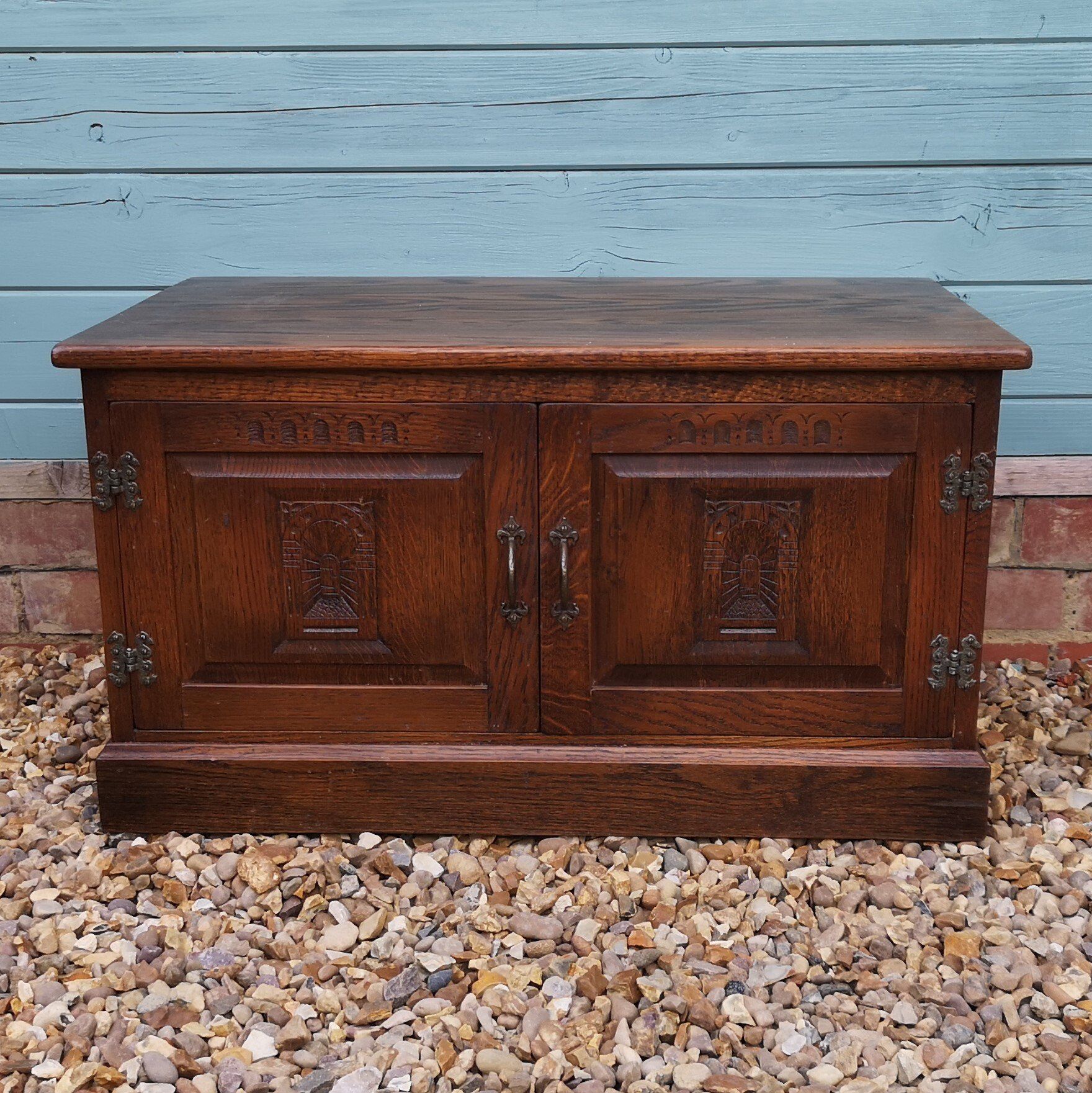 A wooden cabinet is sitting on a pile of gravel in front of a blue wall.