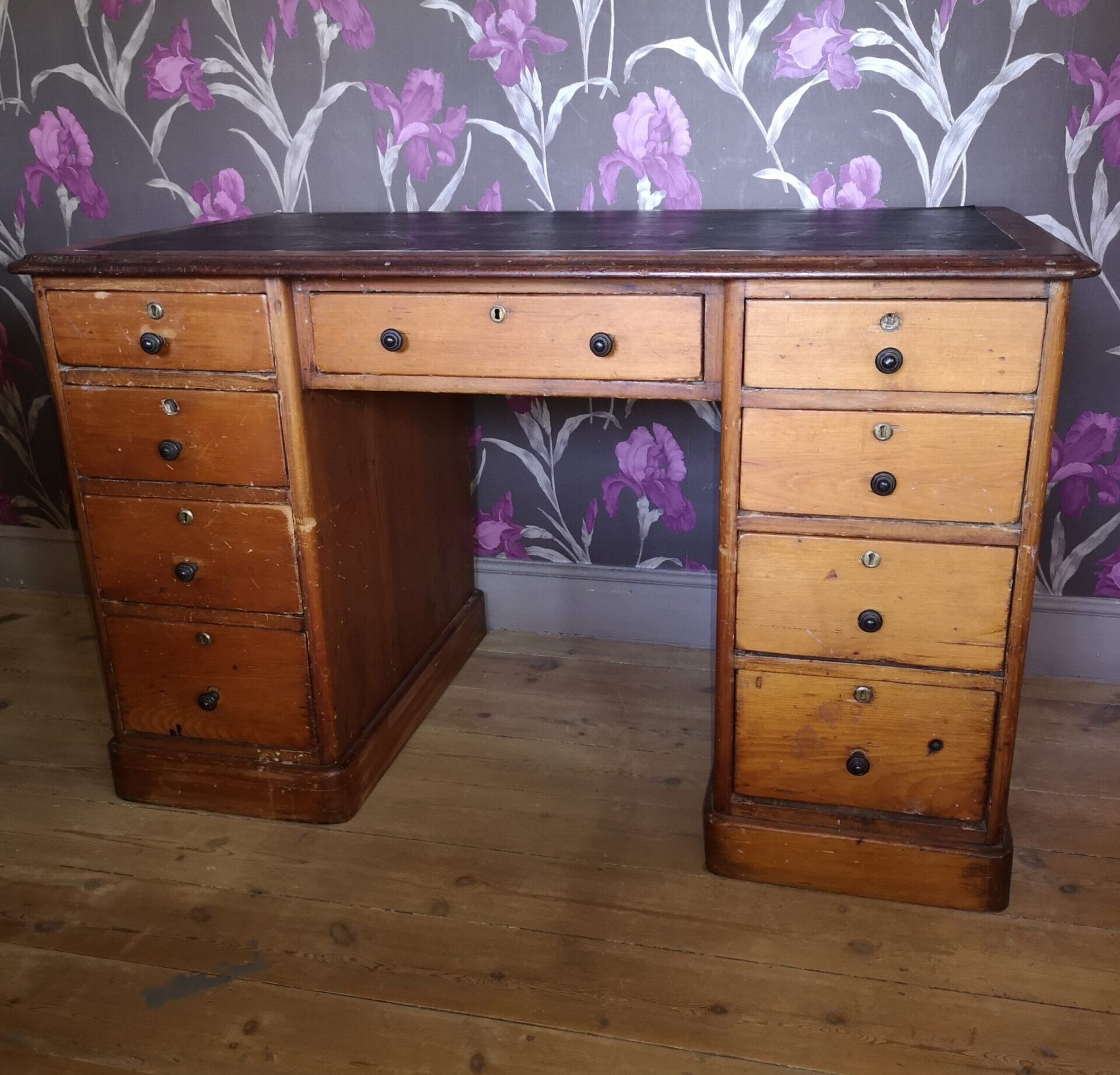 A wooden desk with purple flowers on the wall behind it