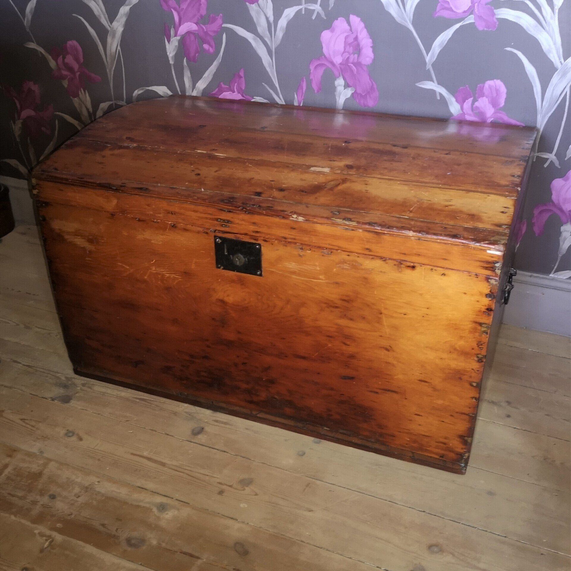 A wooden trunk is sitting on a wooden floor in front of a wall with flowers on it.