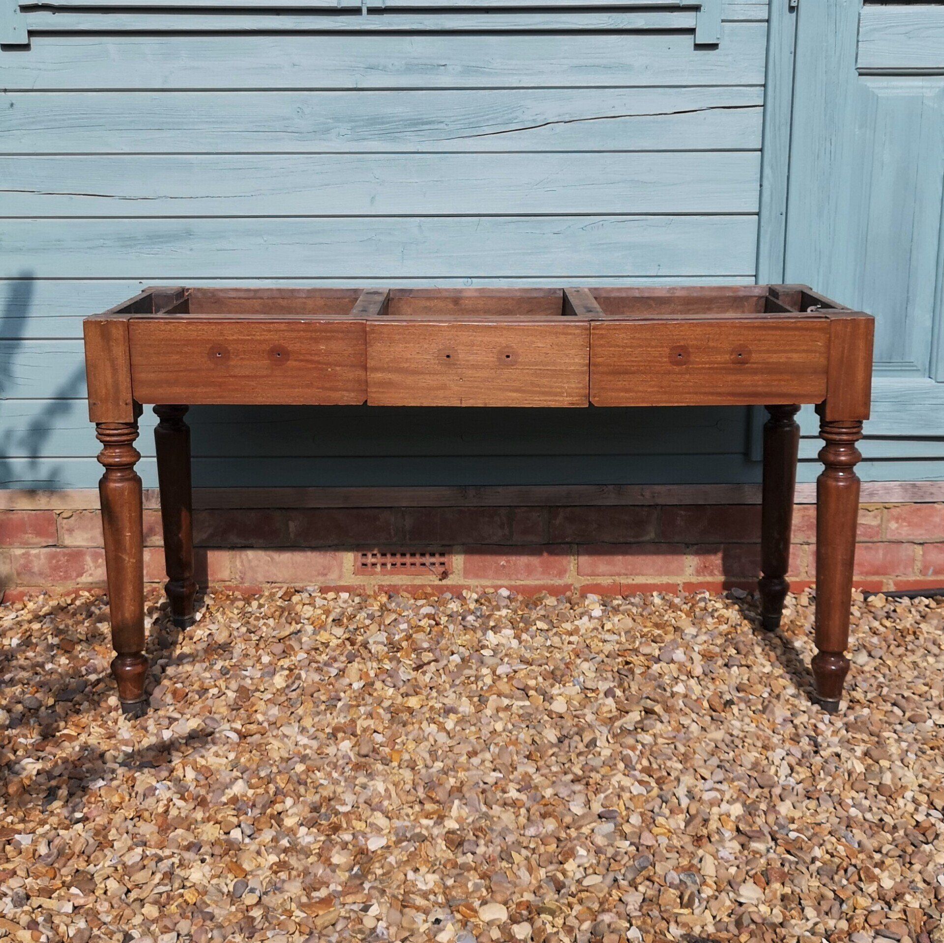 A wooden table is sitting on gravel in front of a blue building