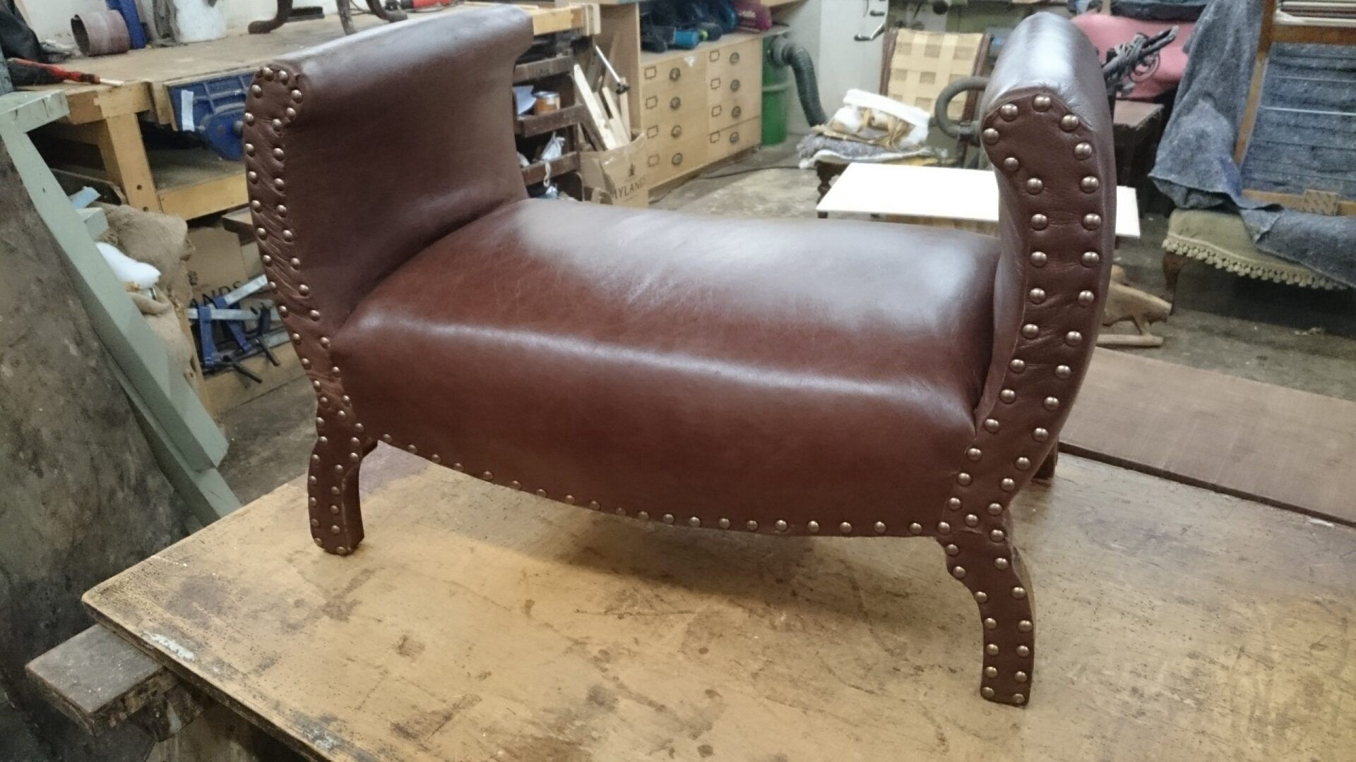 A brown leather bench with studs on the arm rests is sitting on a wooden table.