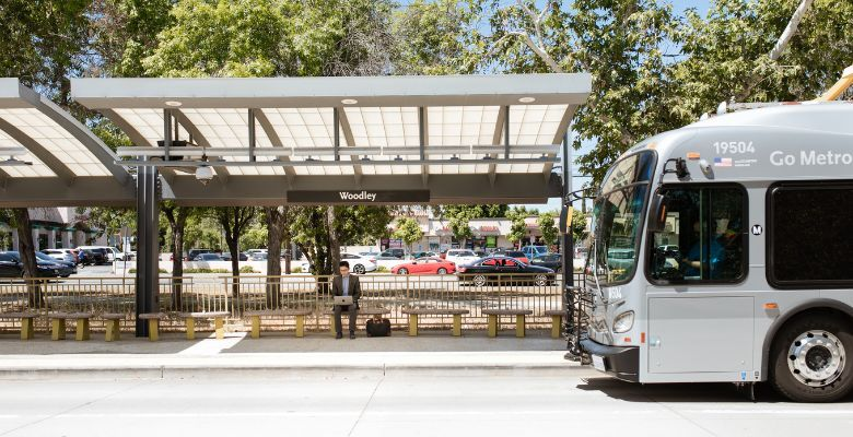 Man waiting at a bus stop under a canopy; a bus pulls up.