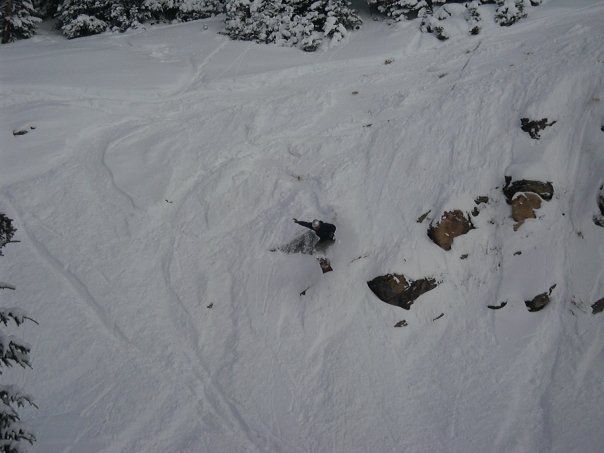 Snowboarder navigating a snowy, rocky mountain face, carving tracks.