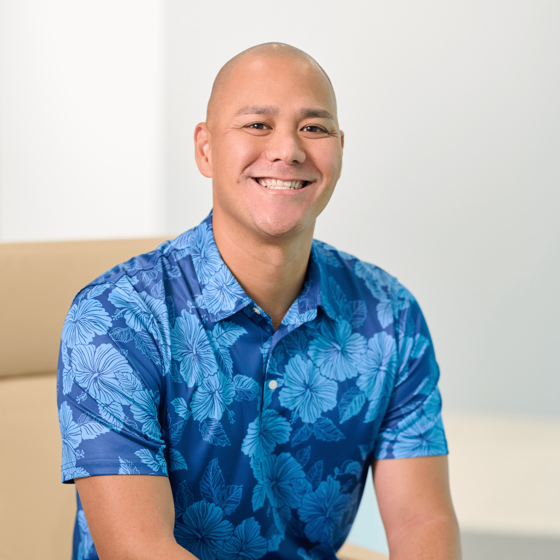 N&K accounting firm Principal Charles Goodin sits in a beige chair wearing a dark blue aloha shirt with lighter blue hibiscus flowers and leaves.