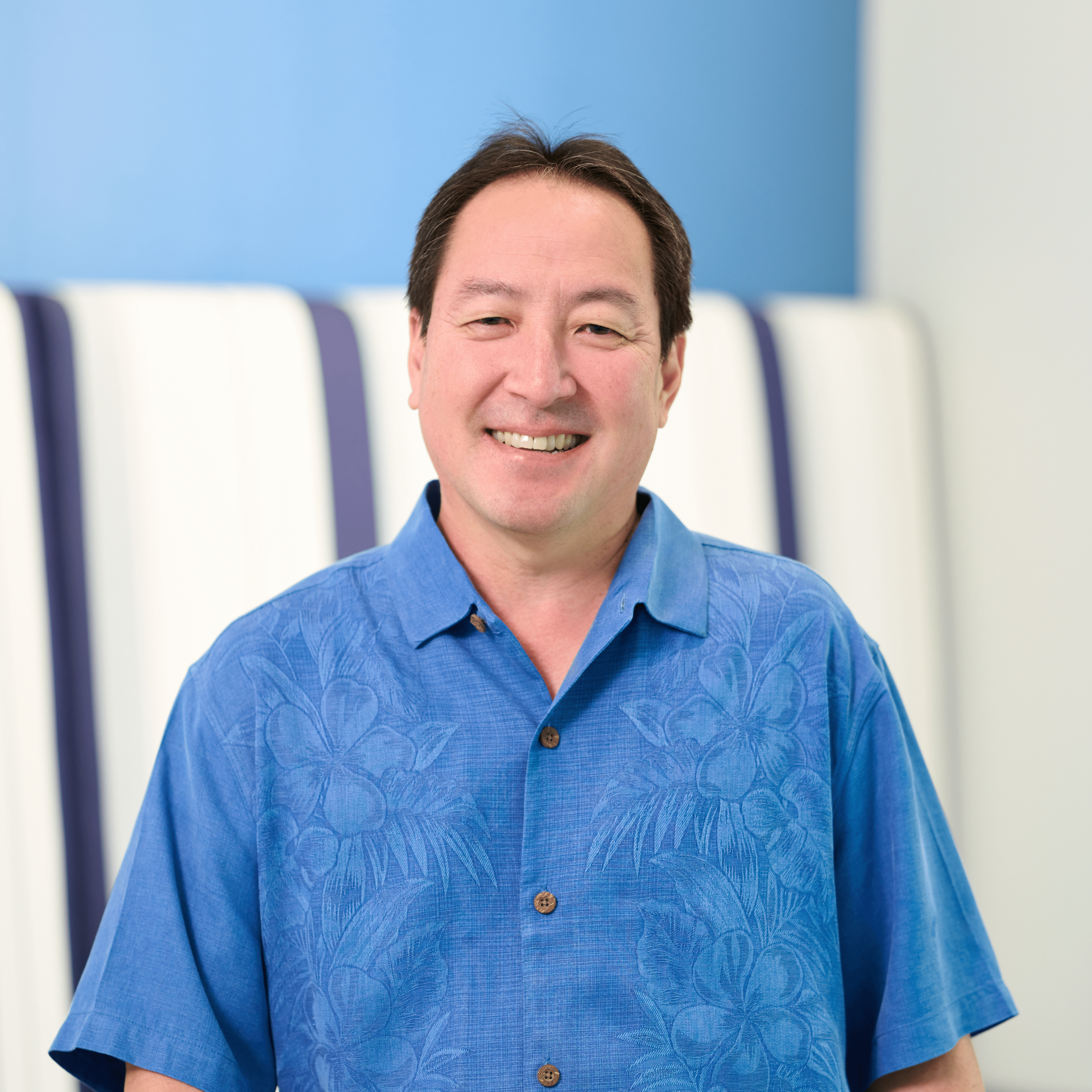 The lead principal of an accounting firm in Oahu, Chad Funasaki, wearing a blue aloha shirt with Hawaiian flowers outlined in lighter blue.