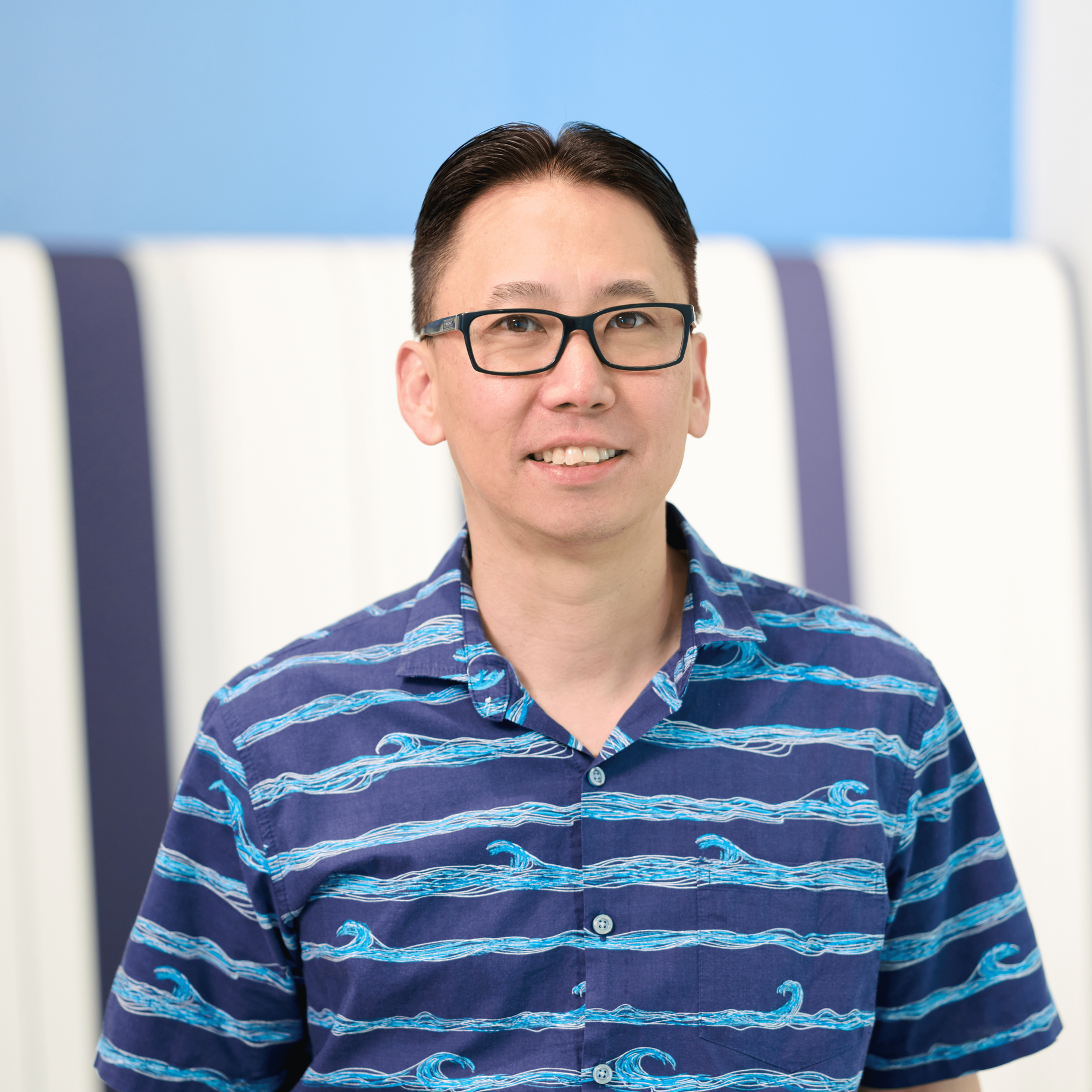 Lead principal of N&K CPA accounting firm Blake Isobe stands in front of a white and blue background wearing glasses and a dark blue shirt with lighter blue waves.