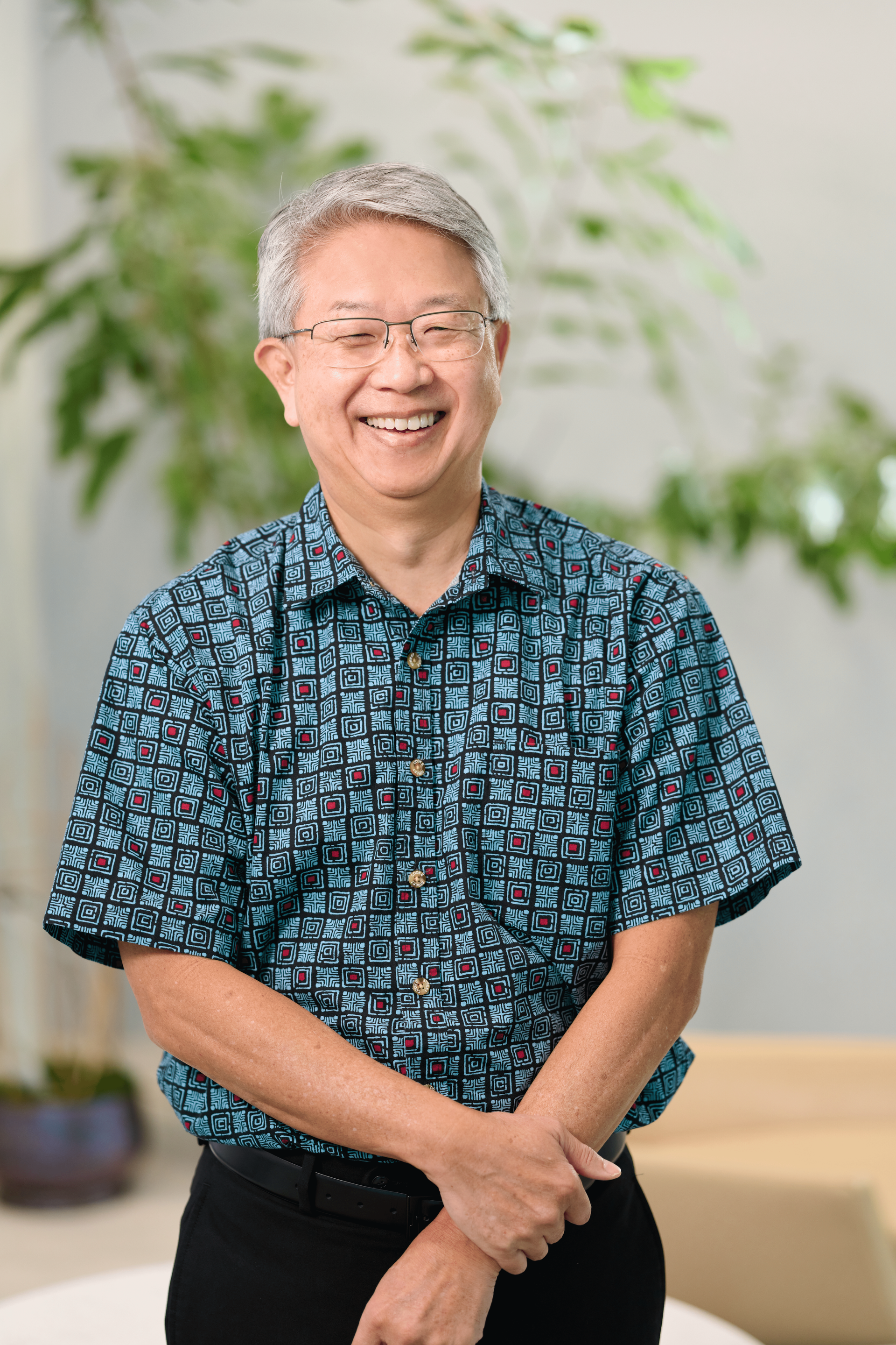 Michael Tanaka standing in front of greenery, wearing a blue and red checkered pattern aloha shirt.