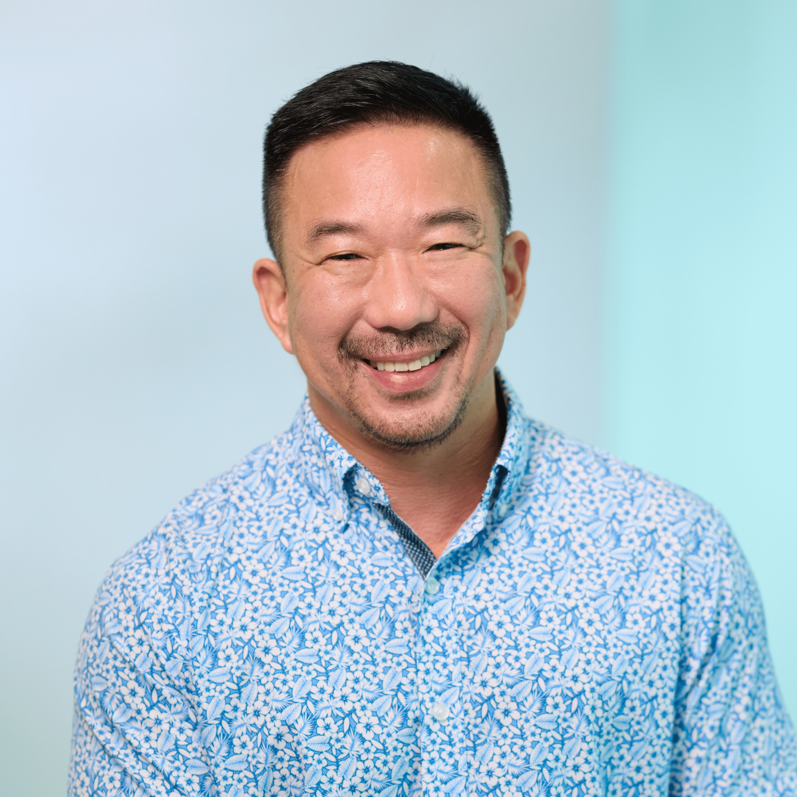 Lead CPA firm in Oahu, Dwayne Takeno, standing in front of a light blue background, wearing a blue and white floral patterned aloha shirt.