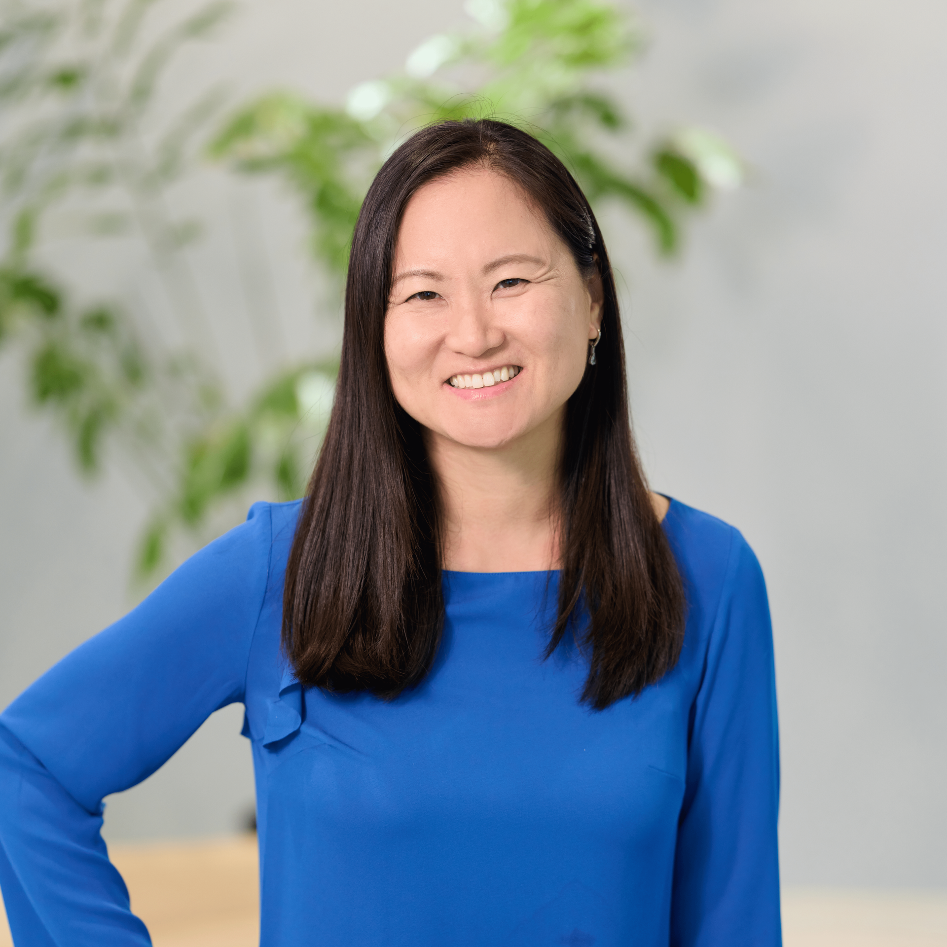 Hawaii accounting firm principal Won Jeong Lee stands in front of an indoor potted tree wearing a blue blouse with flowing sleeves.