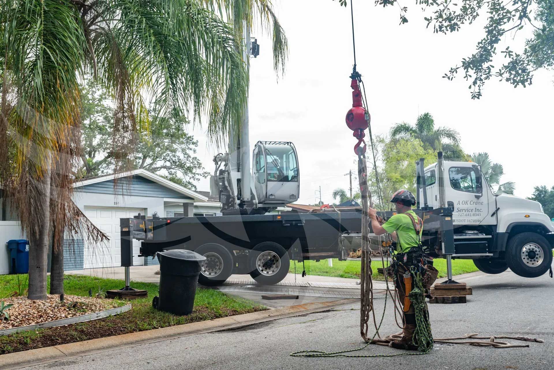 A man is lifting a pole with a crane in front of a truck.