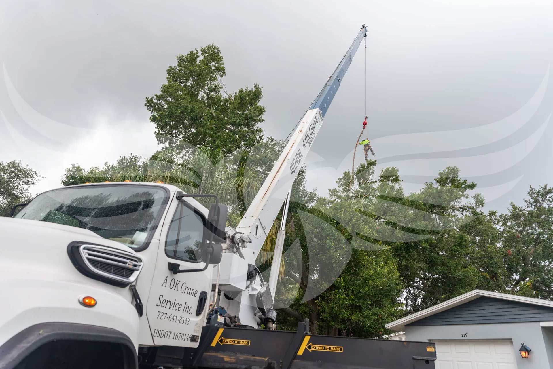 A white truck with a crane attached to it is parked in front of a house.