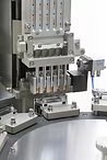 Automated machine filling vials in a factory setting. Silver metal components with a rotating platform.