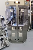 A large, stainless steel tablet press machine with transparent safety shields, in a lab setting.