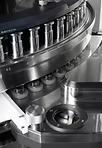 Close-up of a pharmaceutical machine with multiple metal posts and mechanisms, likely filling or manufacturing capsules.