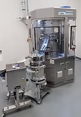 Pharmaceutical tablet press with attached equipment in a laboratory setting.