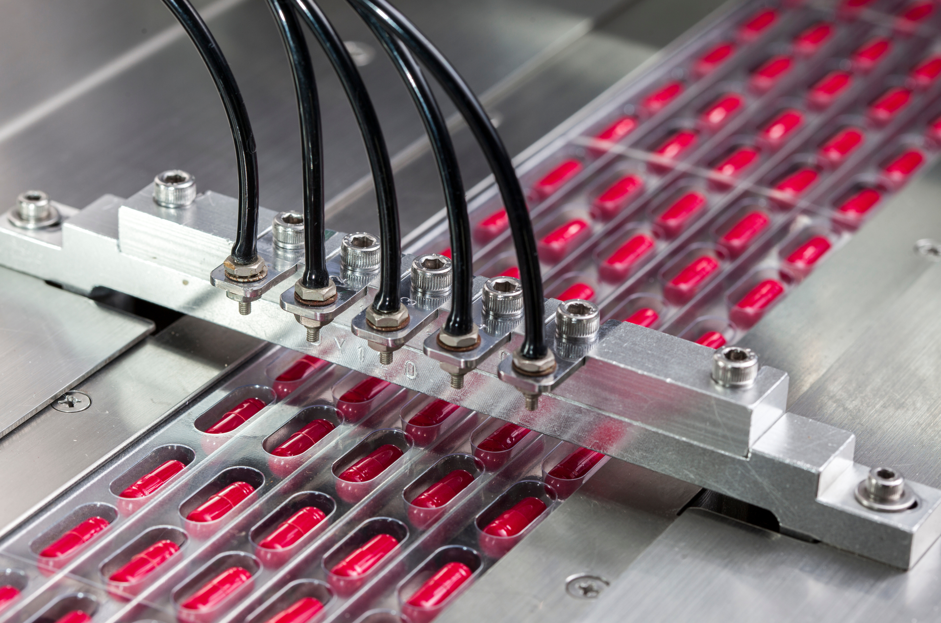 Automated pill packaging machine filling blister packs with red capsules.