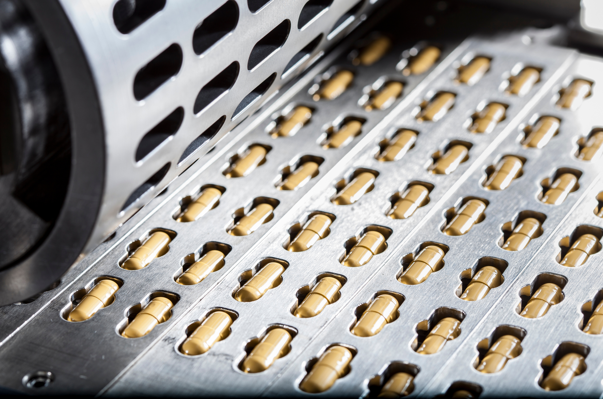 Capsule pills moving through a metal conveyor belt in a pharmaceutical factory.