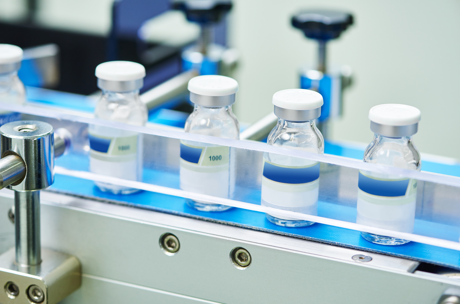 Vaccine vials on a blue conveyor belt in a manufacturing setting.