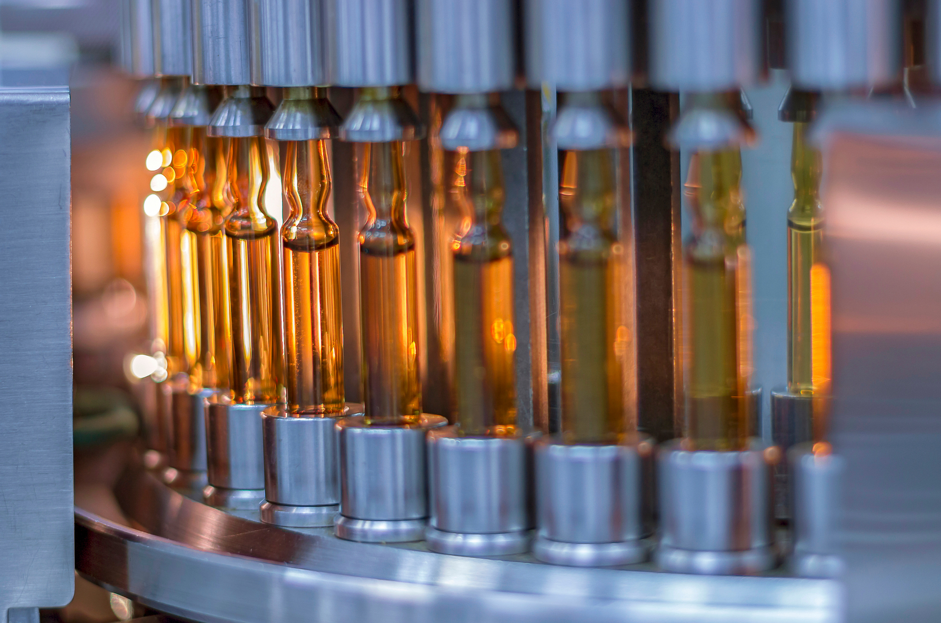 Row of amber vials being filled by automated machinery in a factory setting.