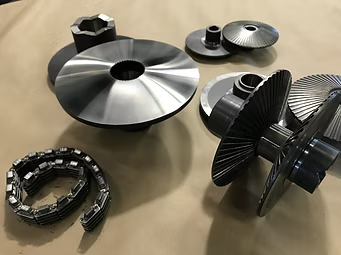 Metal gears and parts, including a drive belt, set on a beige surface.