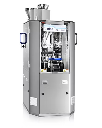 Capsule filling machine, silver, with clear panels showing internal components, in a pharmaceutical setting.