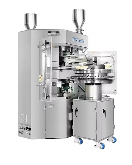 Tablet press machine, silver, with hoppers and rotating table, in a pharmaceutical setting.