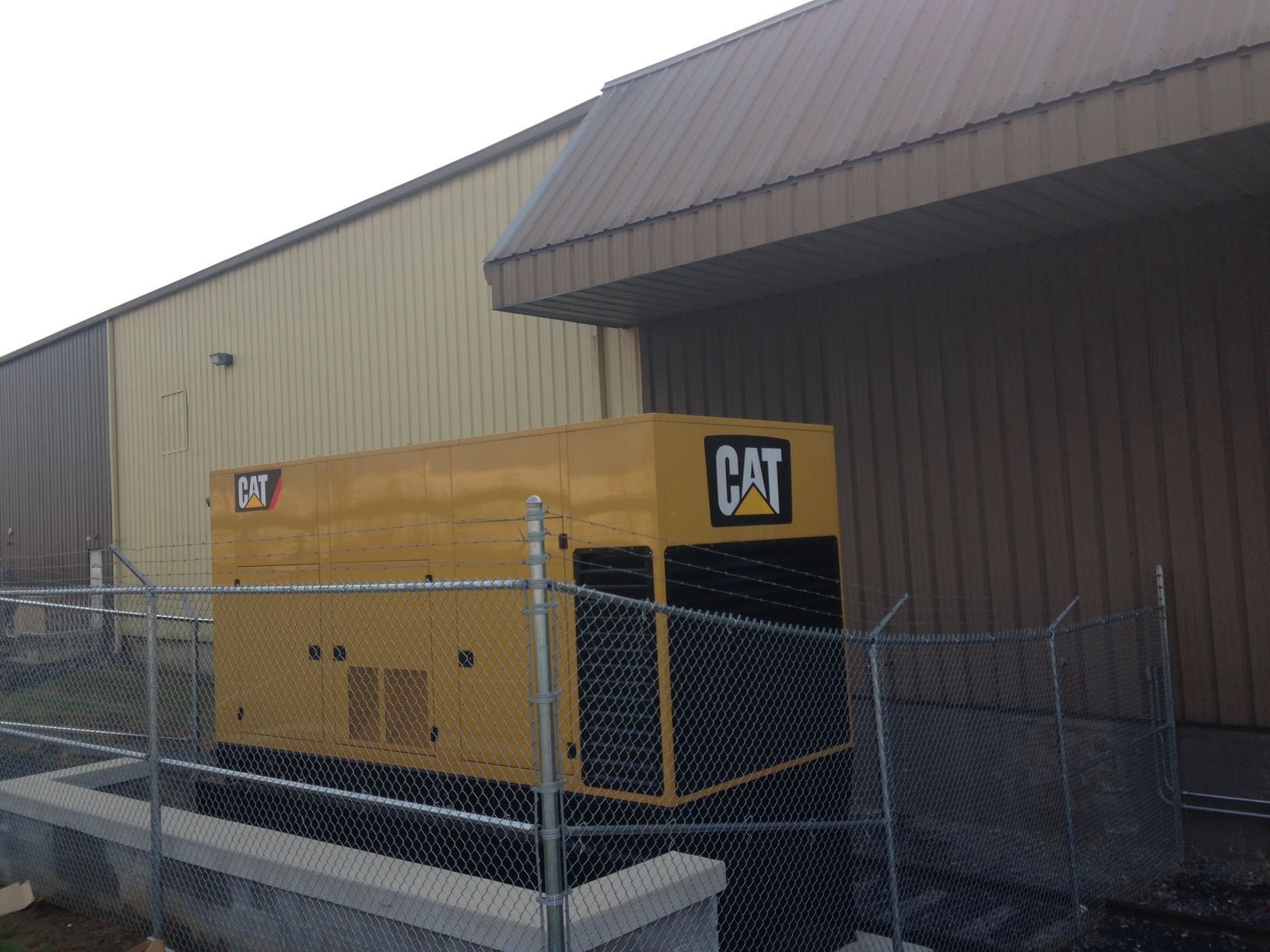 A yellow cat generator is behind a chain link fence