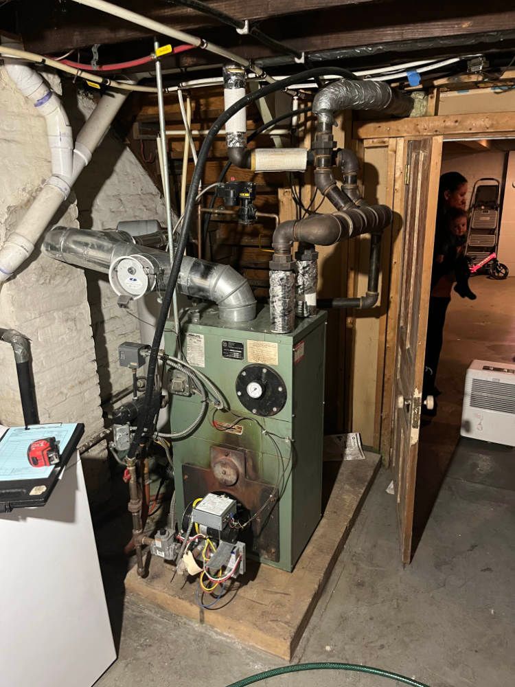 A green boiler is sitting in a basement next to a door.