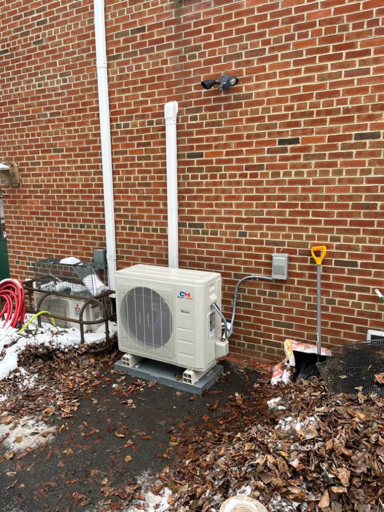 A white air conditioner is sitting on the side of a brick building.