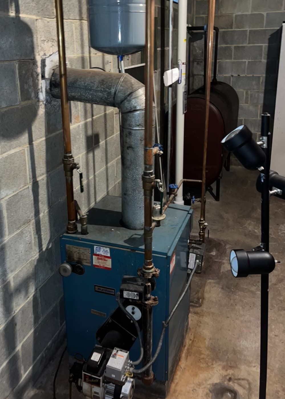 A blue boiler is sitting in a basement next to a brick wall.